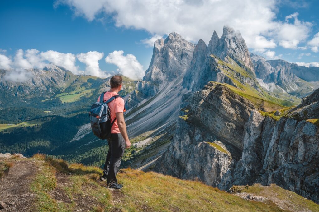 A man with backpack enjoy landscape of Seceda peak in Dolomites Alps, Odle mountain range, South