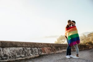 Gay couple wrapped in a gay pride flag kissing on a road in the mountains