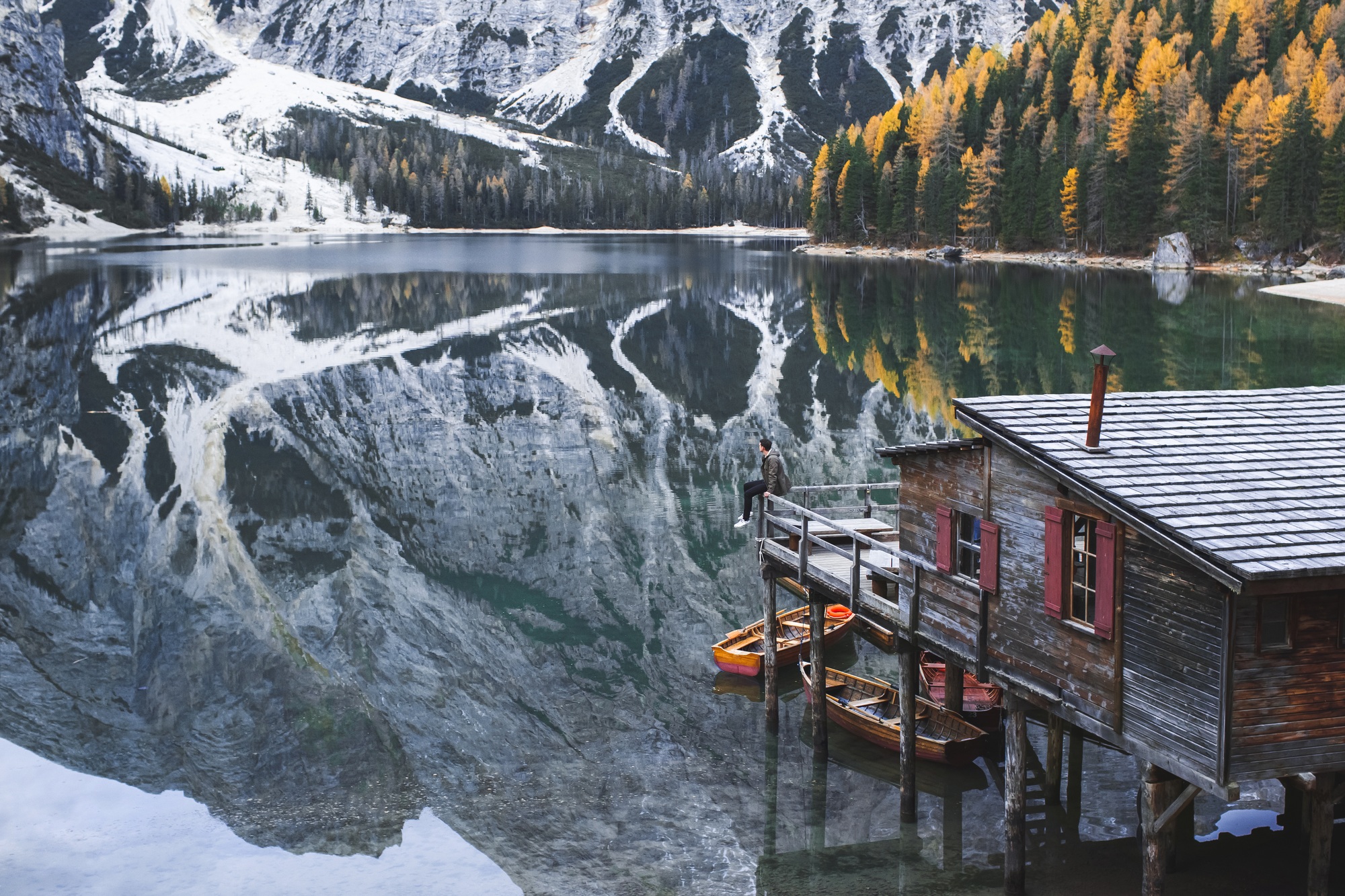 Male person sitting with amazing autumn view of famous tourist landmark Lago di Braies in Italy