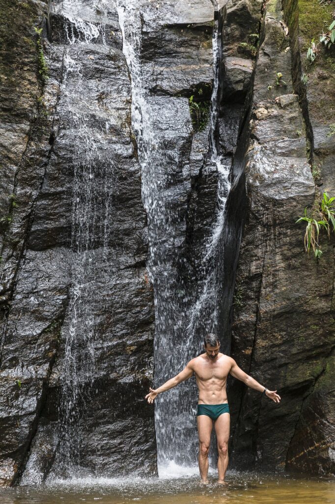 Mature man standing with open arms in front of waterfall, Tijuca Forest, Rio de Janeiro, Brazil