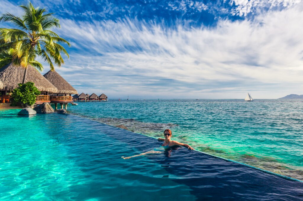 Woman in the infinity pool in exotic island resort with bunalows