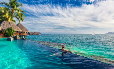 Woman in the infinity pool in exotic island resort with bunalows