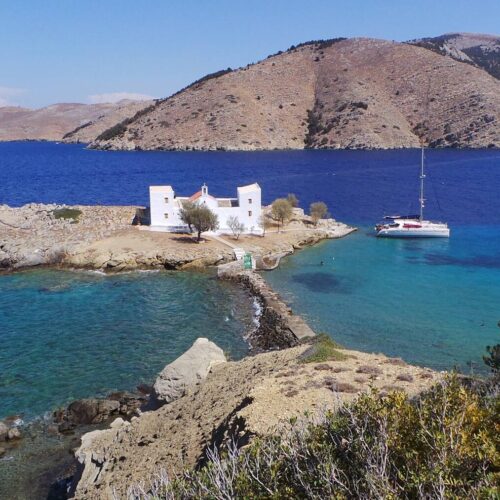 Private catamaran beside the rocky shoreline and chapel of Alimia, Greece