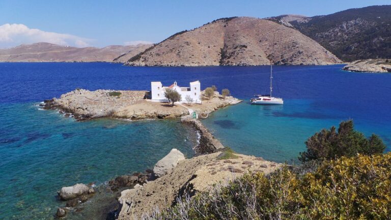 Private catamaran beside the rocky shoreline and chapel of Alimia, Greece